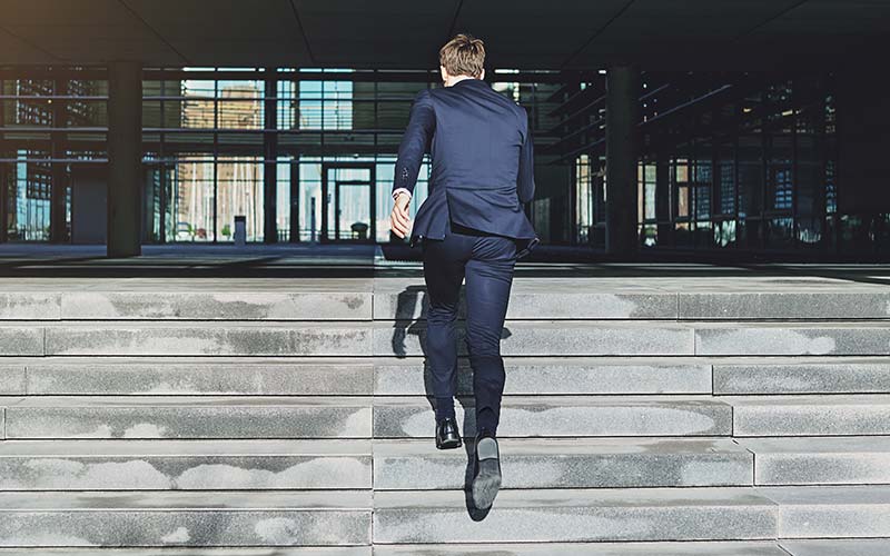 business person running up concrete steps to office building