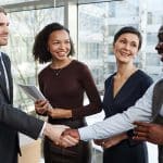 sales professional shakes hands with new clients smiling to highlight emotional intelligence in sales