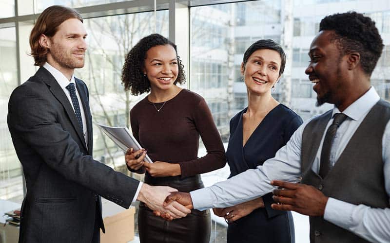 sales professional shakes hands with new clients smiling to highlight emotional intelligence in sales